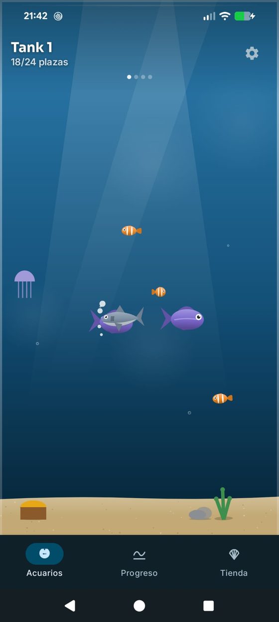 The FocusReef aquarium screen, showing Tank 1 with 18 of its 24 slots filled by clownfish, a jellyfish and two larger fish over a sandy floor.